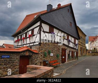 Historisches Fachwerkhaus in Kirchgaesschen Colditz: Traditionelle Architektur mit Steinfuß, Schiefergiebel und Blumen in Sachsen Stockfoto