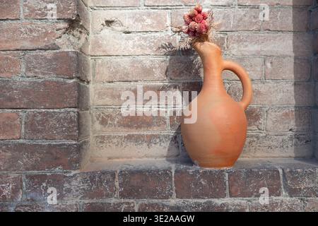 Horizontale Aufnahme einer Terrakotta-Tonkanne mit getrockneten Blüten in einer Mauernische mit großem Kopierraum links. Stockfoto