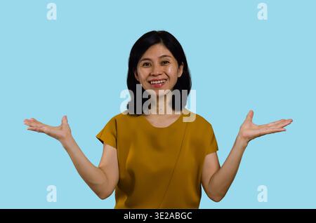 Zeigt asiatische Frau mit offenen Handflächen als Kopierraum für zwei Produkte. Asiatische Frau isoliert auf blauem Hintergrund. Glückliches lächelndes multirassisches asiatisches weibliches M Stockfoto