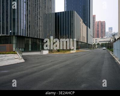 Leere, breite asphaltierte Straße, die zu modernen Geschäftsgebäuden aus dunklem Glas unter einem bewölkten Himmel führt. Repräsentiert Gewerbeimmobilien, corporat Stockfoto