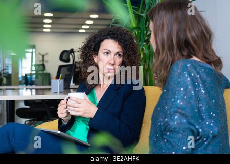 Zwei Geschäftsfrauen, die sich in einer Pause im Büro bei einem Kaffee unterhalten Stockfoto