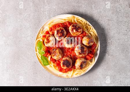 Ein Teller mit klassischen Spaghetti, garniert mit gebräunten Fleischbällchen und reichhaltiger Tomatensauce auf einem leichten Keramikgericht. Stockfoto
