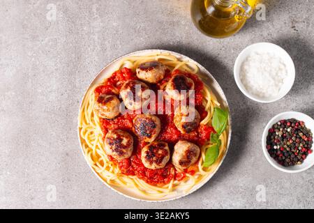 Ein Teller mit klassischen Spaghetti, garniert mit gebräunten Fleischbällchen und reichhaltiger Tomatensauce auf einem leichten Keramikgericht. Stockfoto