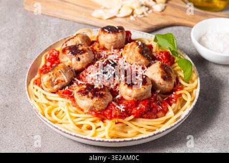 Ein Teller mit klassischen Spaghetti, garniert mit gebräunten Fleischbällchen und reichhaltiger Tomatensauce auf einem leichten Keramikgericht. Stockfoto