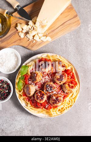 Ein Teller mit klassischen Spaghetti, garniert mit gebräunten Fleischbällchen und reichhaltiger Tomatensauce auf einem leichten Keramikgericht. Stockfoto