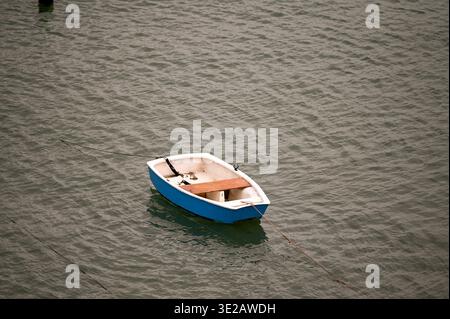 Blaues und weißes Holzfischboot, das in ruhigen Küstengewässern mit Seilanker vertäut ist Stockfoto