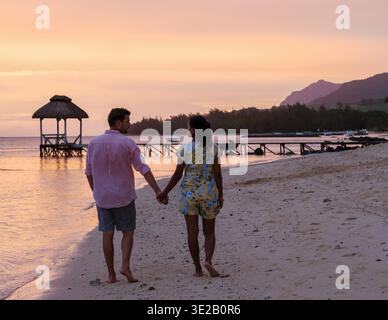 Ein paar Spaziergänge Hand in Hand an einem ruhigen Strand in Mauritius, umgeben von atemberaubenden Sonnenuntergangsfarben. Die Atmosphäre strahlt Romantik aus, perfekt für einen luxuriösen Urlaub. Stockfoto