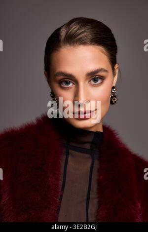 Die schöne Frau zeigt ihre Eleganz mit atemberaubenden Ohrringen und einem glamourösen Look in Burgunderrot. Stockfoto