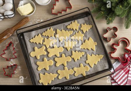Pfanne voller ungebackener Lebkuchenkekse. Weihnachtskuchenmann und Tannen auf Pfanne. Draufsicht. Hausgemachtes traditionelles Rezept Stockfoto