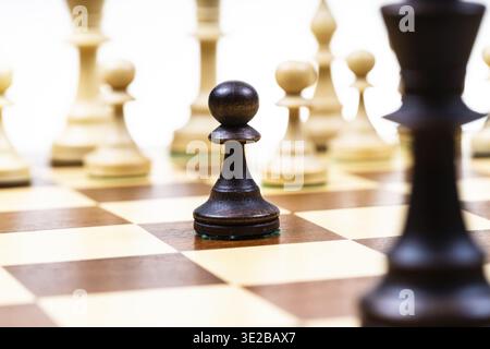 Angriff auf schwarzen Bauern und Königin gegen weiße Schachfiguren im Hintergrund auf hölzernem Schachbrett Nahaufnahme (Fokus auf die schwarze Schachfigur) Stockfoto