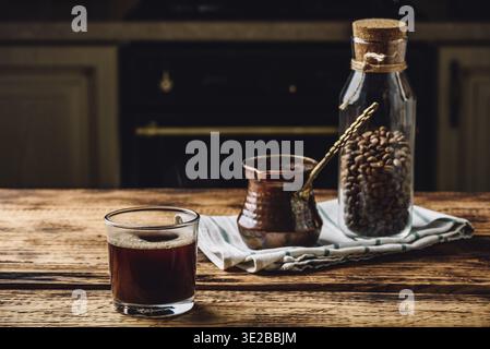Essen, frisch gebrühter türkischer Kaffee im Trinkglas. Cezve und ein Glas gerösteter Kaffeebohnen Stockfoto