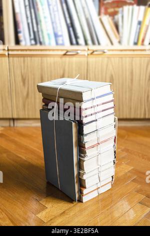 Stapel altes Buch, das mit Garn gebunden ist, auf Holzboden in der Nähe des Bücherregals Stockfoto