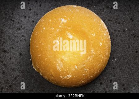 Draufsicht auf ein einzelnes rundes Stück Palmzucker auf schwarzer Keramikplatte Stockfoto