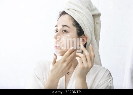 Nahaufnahme einer Frau, die vor einem Spiegel in ihrem Haus Creme auf ihr Gesicht aufträgt Stockfoto