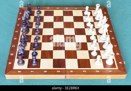 Seitenansicht des hölzernen Schachbretts mit Schachfiguren in Startposition auf grünem Baizentisch Stockfoto