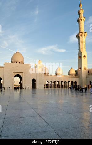 Während des Sonnenuntergangs spazieren die Menschen im Innenhof der Scheich-Zayed-Moschee in Abu Dhabi und genießen die Architektur und Atmosphäre. Stockfoto