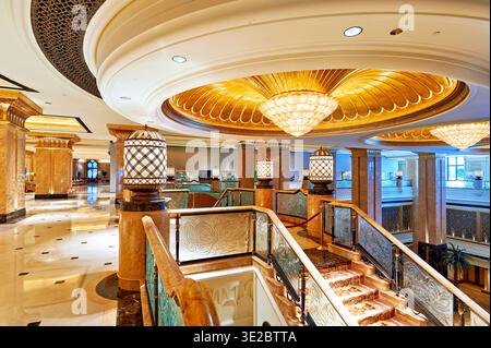 Gäste laufen durch die Halle des Emirates Palace Hotel in Abu Dhabi. Der Innenraum zeigt kunstvolle Details und helle Beleuchtung im gesamten Raum. Stockfoto