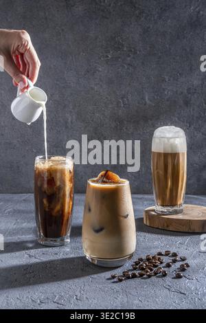 Milch wird auf einem dunklen Tisch in Eiskaffee gegossen. Eiskaffee in einem großen Glas mit Sahne und Kaffeebohnen. Kaltes Kaffeegetränk auf einem dunklen Ba Stockfoto