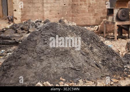 Kano, Nigeria - 27. Januar 2024: Der Blick auf einen dunklen Haufen steht im Kontrast zum verwitterten Ziegelstein der Feuerwehr Dakata auf dem Fatima Market, Kano, Nigeria. Stockfoto