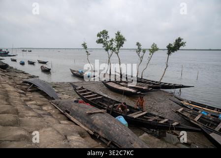 Satkhira, Bangladesch - 25. April 2025: Blick auf verwitterte Holzboote ruhen auf dem matschigen Ufer, im Kontrast zum grauen Himmel und fernen Horizont. Stockfoto