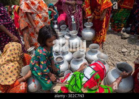 Satkhira, Bangladesch - 25. April 2025: Blick auf Frauen und Kinder, die sich um eine Sammlung von silbernen Töpfen versammeln, deren leuchtende Saris im Kontrast dazu stehen Stockfoto