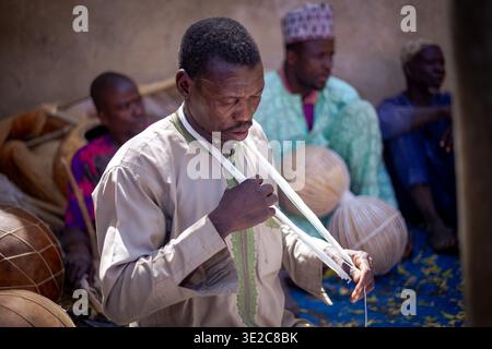 Luftaufnahme eines Mannes mit einer weißen Schnur um den Hals, umgeben von Trommeln und anderen Menschen, Kano, Nigeria. Stockfoto