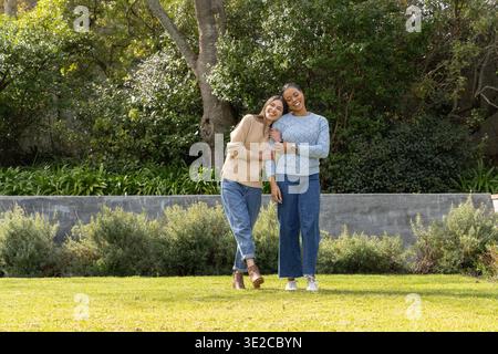 Verschiedene Freundinnen stehen auf dem Rasen in der Nähe einer niedrigen Betonwand, tragen Pullover und Jeans. Im Freien, Natur, Grün, Garten, Park, Glück Stockfoto