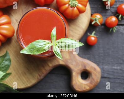 Frischer Tomatensaft im Glas und reife Tomaten auf dem Hintergrund. Tomaten Frisch. Tomatensaft und Basilikum Stockfoto