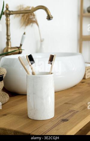 Nahaufnahme von drei Bambuszahnbürsten in einem Glas auf Holztisch im Badezimmer Stockfoto
