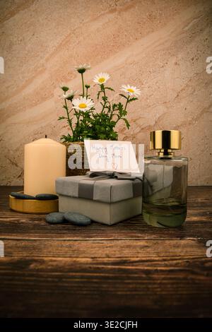 Stillleben zum Muttertag mit Gänseblümchen, handgeschriebener Karte, Kerze, Parfümflasche und verpacktem Geschenk auf rustikalem Holz, gestaltet für Spa, Schönheit und Feier Stockfoto