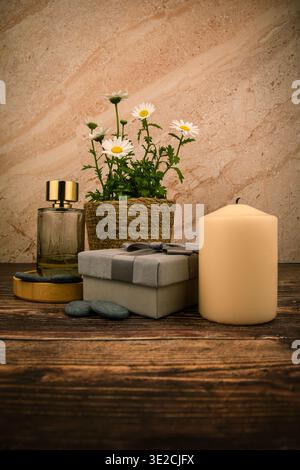 Gänseblümchen, Parfümflasche, Kerze und Geschenkverpackungen auf rustikalem Holz, eine raffinierte Spa-Komposition zum Muttertag mit warmen Tönen und Kopierraum. Stockfoto