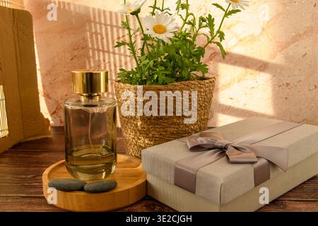Sonnendurchflutetes Stillleben mit Parfümflasche, Gänseblümchen und Geschenkverpackungen auf rustikalem Holz, ideal für Muttertag, Schönheit, Wellness und Spa-Konzepte. Stockfoto