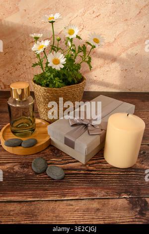 Gänseblümchen, Parfümflasche, Kerze und Geschenkverpackungen auf rustikalem Holz, eine raffinierte Spa-Komposition zum Muttertag mit warmem Licht und Kopierraum. Stockfoto