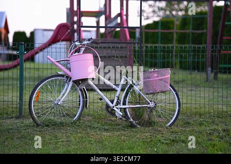 Eine dekorative Gartenanlage aus einem alten Fahrrad mit einem rosafarbenen Blumenkorb und einer Gießkanne. Horizontales Foto Stockfoto