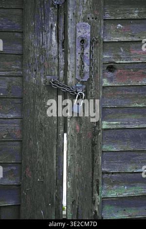 Eine alte Holztür, verschlossen mit einem Vorhängeschloss und einer Kette. Vertikales Foto Stockfoto