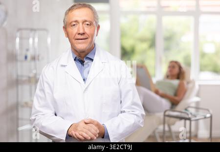 Der ältere Arzt steht in der Klinik und der Patient liegt auf der Couch Stockfoto