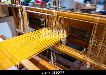 Nahaufnahme eines Webstuhls mit goldenen Garnfäden in einer Textilwerkstatt. Handgefertigte Stoffproduktion und traditionelles Kunsthandwerk mit geringer Tiefe Stockfoto