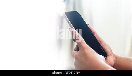 Nahaufnahme von Frauenhänden, die das Smartphone in Profilansicht halten, mit hellem Licht und minimalistischem Kommunikationskonzept Stockfoto