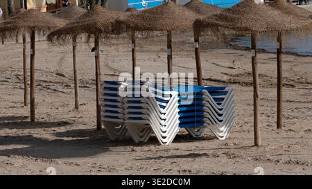 Stapel von Liegestühlen unter Strohschirmen am Sandstrand Stockfoto