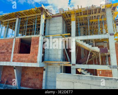 Die Arbeiter sind auf einer Baustelle beschäftigt, auf der ein neues Gebäude gebaut wird. Die Struktur zeigt eine Mischung aus Ziegel und Beton mit Gerüsten Stockfoto