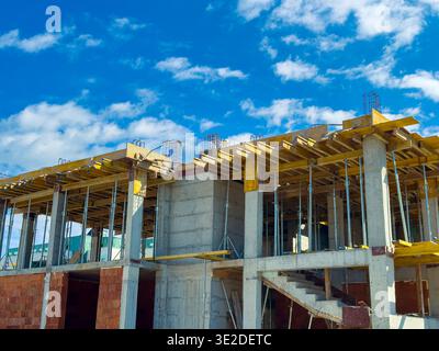 Arbeiter bauen einen Gebäuderahmen mit Beton und Gerüsten. Der Standort ist mit Materialien und Werkzeugen beschäftigt. Das Wetter ist klar und sonnig mit wenig C Stockfoto