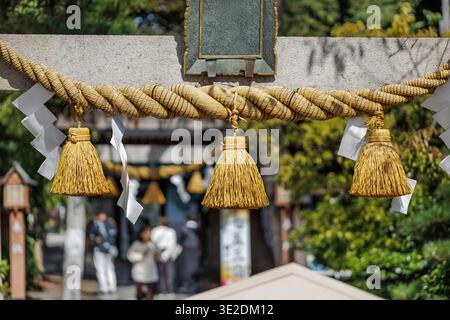 Heiliges Shimenawa-Strohseil und Zickzack-shide-Papier-Streamer hängen am sonnenbeleuchteten Torii-Tor und markieren den Eingang in das heilige Viertel Shinto Shine. Stockfoto