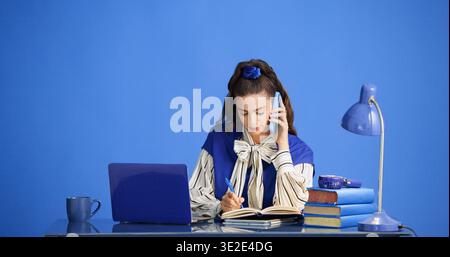 Laptop, Telefonanruf und Geschäftsfrau, die im Studio schreibt, mit Kontakt für Feedback zu kreativen Projekten. Handy, Notizen und Zeitschriftenredakteur auf Handy Stockfoto