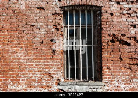 Rechteckiges Fenster mit eisernem Gitter an einer alten, abgesplitteten roten Ziegelwand. Aus der Serie Windows of the World. Stockfoto