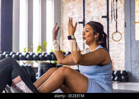 Weibliche Trainingspartnerinnen, die Sit-ups auf dem Fitnessraum im Studio in blauem Set neben Kurzhanteln durchführen Stockfoto