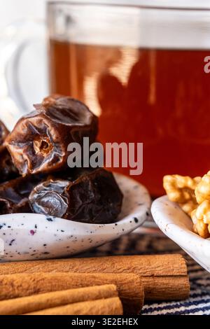 Ein Teller mit Datteln bereit für iftar, begleitet von einem Glas Tee. Die Khudri-Datteln sind dunkel und glänzend und zeigen ihre reiche Textur. Stockfoto