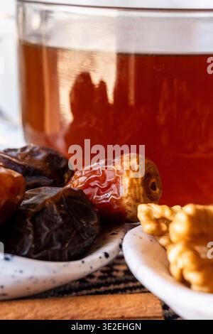 Ein Teller mit Datteln bereit für iftar, begleitet von einem Glas Tee. Die Khudri-Datteln sind dunkel und glänzend und zeigen ihre reiche Textur. Stockfoto