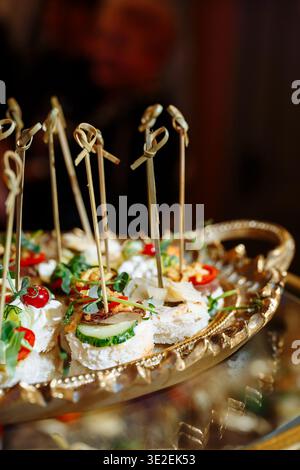 Nahaufnahme einer luxuriösen goldenen Platte mit eleganten Häppchen mit Frischkäse, Gurkenscheiben, Kirschtomaten, Kräutern, Nüssen und künstlerischem Ba Stockfoto