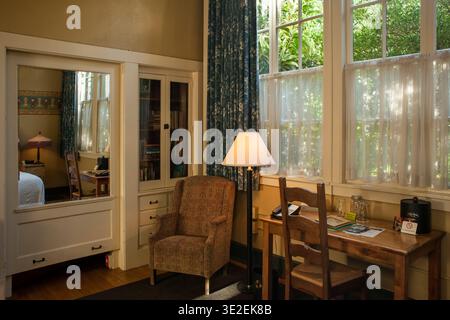 Inneneinrichtung eines gemütlichen Hotelzimmers der Kennedy Elementary School mit Holzschreibtisch, großen Fenstern und einem Sessel in Portland, Oregon Stockfoto