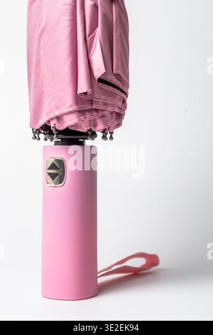 Kompakter rosafarbener Regenschirm mit glattem Stoff und rosafarbenem Griff mit ergonomischen Knöpfen zum Öffnen und Schließen. Metallisches Gehäuse und wasserdichtes Material Stockfoto
